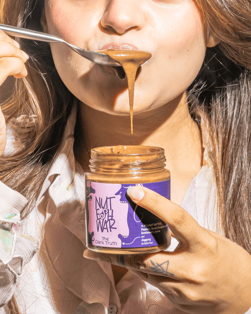 Woman tasting The Dark Truth nut butter from a spoon while holding the jar